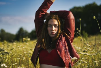 Photo of Woman in Red Leather Jacket and Red Crop Top Standing in Flower Field Raising Her Hands