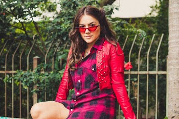 Photo of Woman in Red Leather Jacket and Sunglasses Sitting In Front of Grey Metal Fence