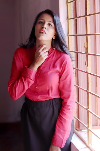 Photo of Woman in Red Long-sleeved Shirt and Black Skirt Standing By Window With Metal Frame