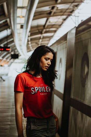 Photo of Woman in Red T-shirt and Blue Jeans Standing in Subway Platform Looking Down 