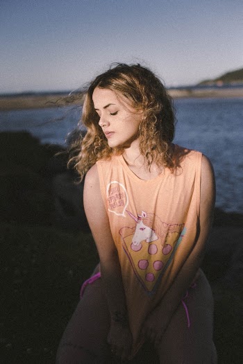 Photo of Woman in Sleeveless T-shirt Posing Near Body of Water With Her Eyes Closed