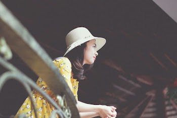 Photo of Woman in Sun Hat and Floral Dress Leaning on Metal Railing Looking Out
