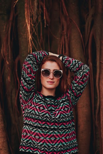 Photo of Woman in Sunglasses Posing with Her Hands Over Her Head While Standing In Front Tree