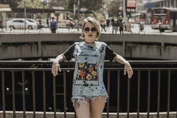 Photo of Woman in Sunglasses, T-shirt, and Denim Shorts Leaning on Metal Railing Posing