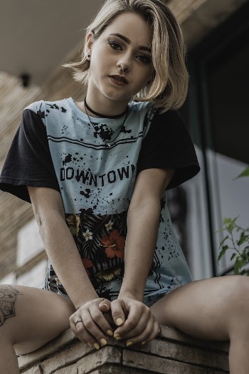 Photo of Woman in Teal and Black T-shirt Sitting on Concrete Edge Posing