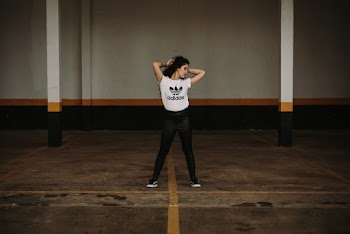 Photo of Woman in White Adidas Shirt Posing in the Middle of a Parking Lot