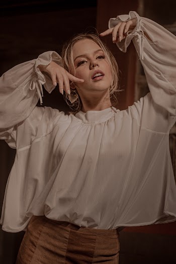 Photo of Woman in White Blouse and Brown Skirt Posing with Her Arms Raised
