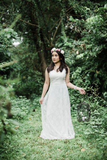 Photo of Woman in White Dress and Flower Crown Holding Bird Cage Candle Holder Standing in the Middle of the Woods