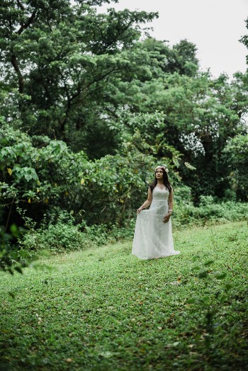 Photo of Woman in White Dress and Flower Crown Standing Alone in Grass Field While Looking up