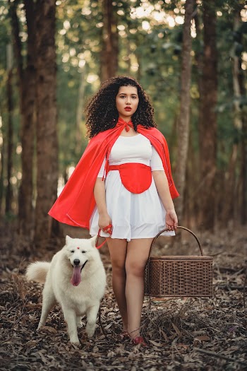 Photo of Woman in White Dress and Red Cape Posing with White Dog While Carrying a Basket