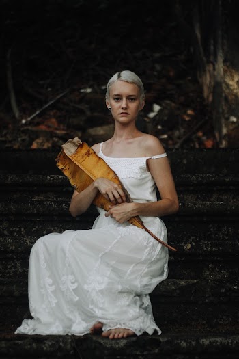 Photo of Woman in White Dress Sitting on Concrete Staircase Holding Dry Banana Leaf