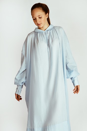 Photo of Woman in White Long-sleeved Night Dress Posing While Looking Down In Front of White Background