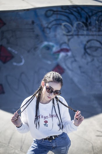 Photo of Woman in White Long-sleeved Shirt Standing Inside Skate Pit While Holding Her Braided Hair