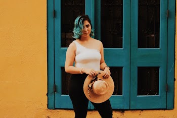 Photo of Woman in White One-sleeved Top and Black Jeans Holding Brown Sun Hat