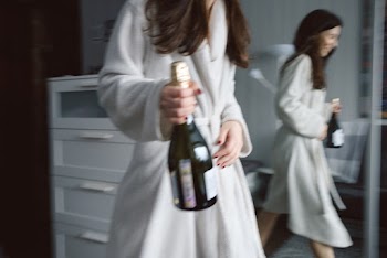 Photo of Woman in White Robe Carrying a Wine Bottle