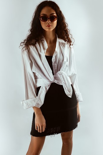 Photo of Woman in White Shirt, Black Dress, and Sunglasses Posing In Front of White Background