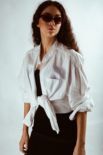 Photo of Woman in White Shirt, Black Dress, and Sunglasses Posing In Front of White Background