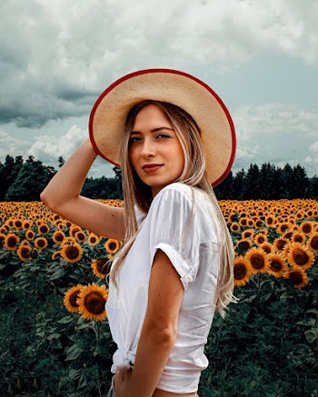 Photo of Woman in White Short-sleeved Crop-top and Brown Sun Hat Posing by Sunflower Field