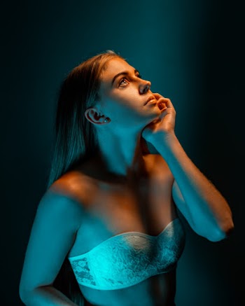Photo of Woman in White Strapless Lace Bra Posing in Front of Blue Background While Looking Up
