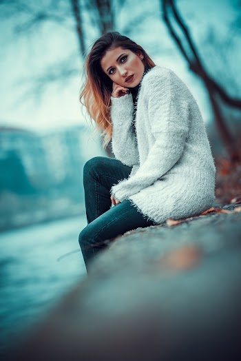 Photo of Woman in White Sweater Sitting on Concrete Riverbank