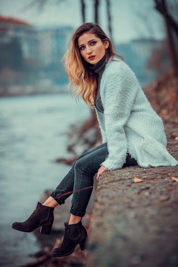 Photo of Woman in White Sweater Sitting on Concrete Riverbank