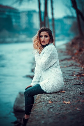Photo of Woman in White Sweater Sitting on Concrete Riverbank