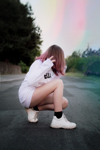 Photo of Woman in White Sweatshirt Dress Squat Posing in the Middle of a Road with Her Hair Covering Her Face