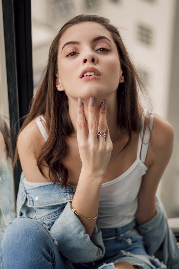 Photo of Woman in White Top and Denim Outfit Posing With Her Fingers Under Chin