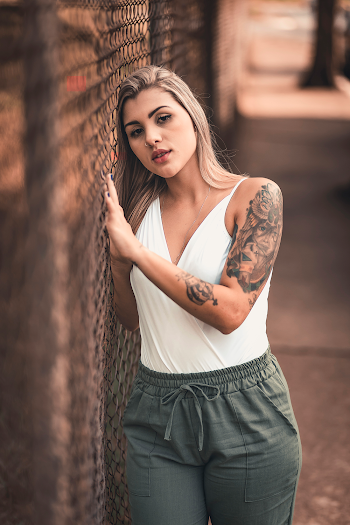 Photo of Woman in White Top and Grey Pants Leaning on Chain-link Fence