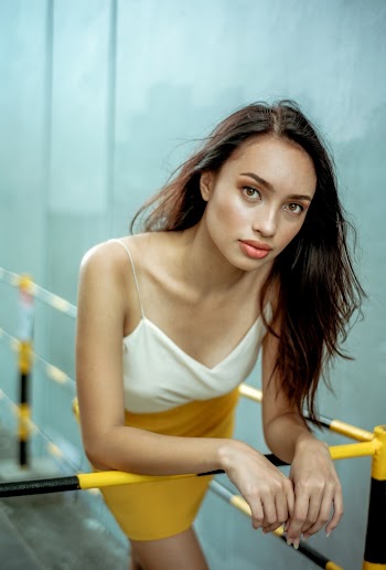 Photo of Woman in White Top and Yellow Dress Leaning Forward on Metal Railing Posing