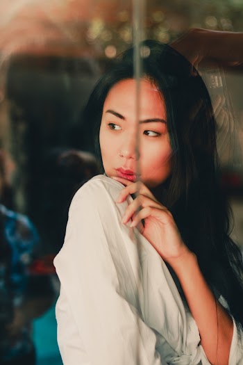 Photo of Woman in White Top Posing Behind Glass Window Looking Outside