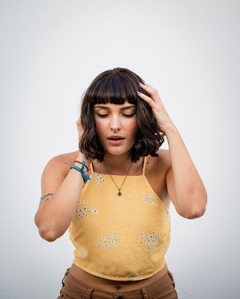 Photo of Woman in Yellow Crop Top Standing in Front of Wall With Her Eyes Closed