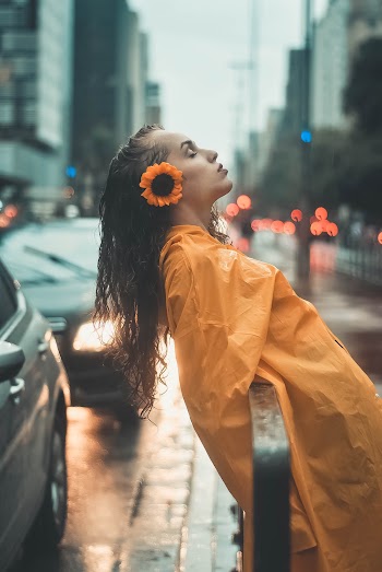 Photo of Woman in Yellow Raincoat Leaning on Black Metal Railing by Sidewalk