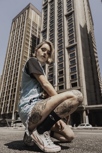 Photo of Woman Kneeling on Ground Posing with High-rise Building in the Background