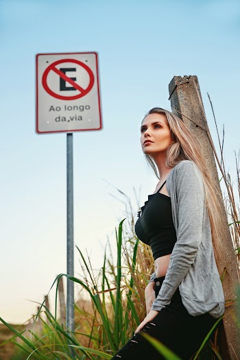 Photo of Woman Leaning Against a Concrete Post Beside a Road Signage Posing While Looking Away