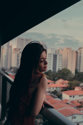 Photo of Woman Leaning on Metal Railing Posing with Her Eyes Closed