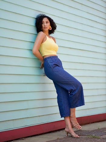 Photo of Woman Leaning on Wall of Wooden House Posing While Looking Away