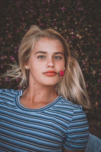 Photo of Woman Lying Down while Biting Red Flower