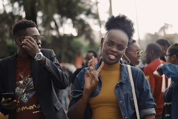 Photo of Woman Posing With Her Tongue Out and Doing the Peace Sign With a Crowd of People in the Background