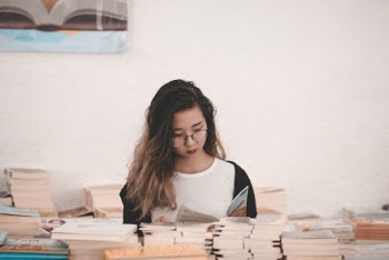 Photo of Woman Reading Book in Room Full of Books