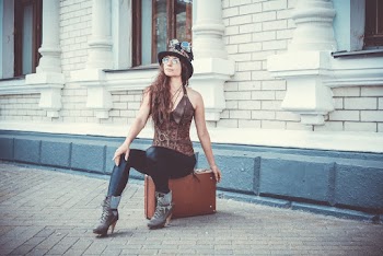 Photo of Woman Sitting on Brown Suitcase In Front of a Building