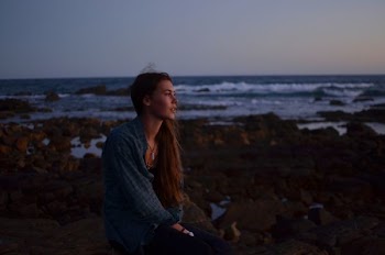 photo of woman sitting on rocks near beach