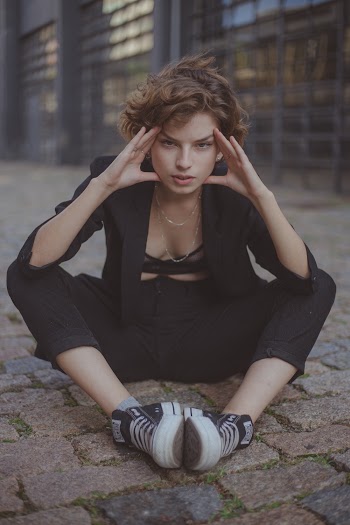 Photo of Woman Sitting on Stone Pavement While Holding Her Temple With Building in the Background