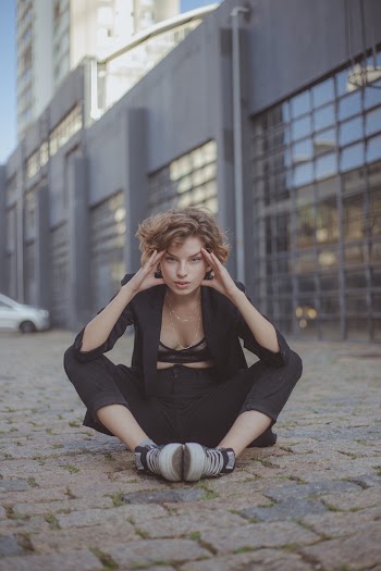 Photo of Woman Sitting on Stone Pavement While Holding Her Temple With Building in the Background