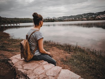 Photo of Woman Sitting on Stone Wall While Looking Towards Lake