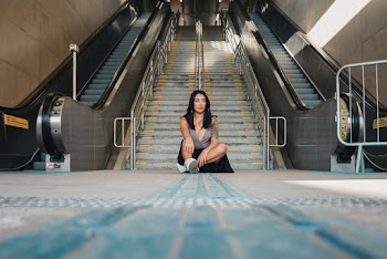 Photo of Woman Sitting on the Ground with Gray Concrete Stairs and Escalators in the Background
