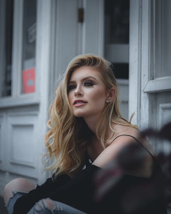 Photo of Woman Sitting Outside Storefront Looking into the Distance 