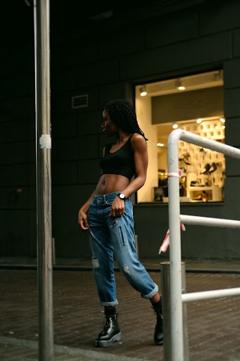 Photo of Woman Standing Across a Store Front in Black Crop Top Holding Her Jeans