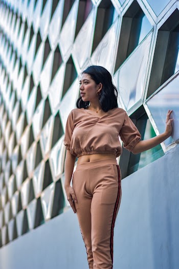 Photo of Woman Standing  in Brown Crop Top and Pants With Her Palm on  Building