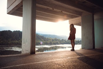 Photo of Woman Standing Under Concrete Building and Body of Water in the Background